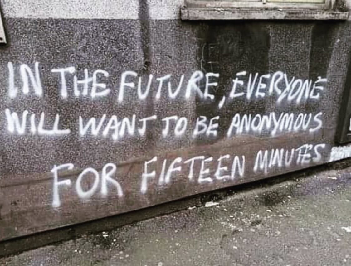 "In the future, everyone will want to be anonymous for fifteen minutes." spray painted on a wall in white paint. It's a play on the (probably misattributed) quote from Andy Worhol, "in the future, everyone will be world famous for fifteen minutes."